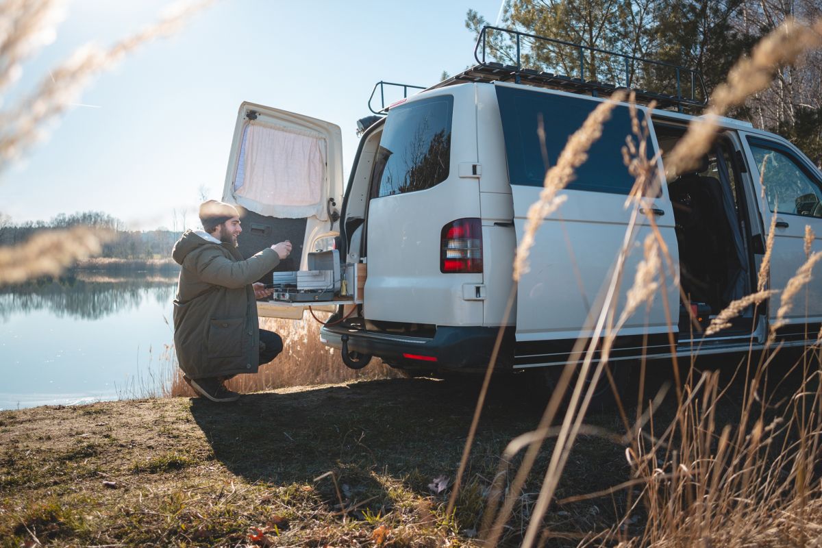 Junger Mann mit umgebautem Camper-Van am See